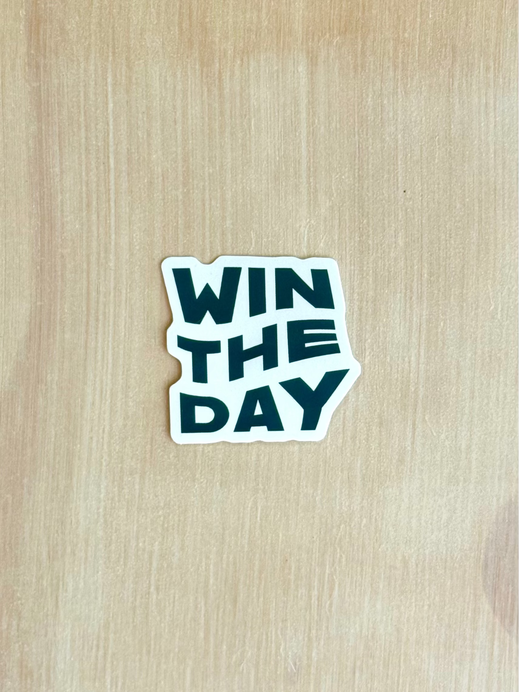Sticker with 'WIN THE DAY' text on a wooden surface